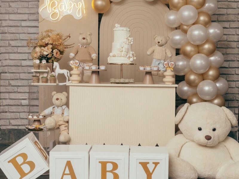 Elegant baby shower setup with Oh Baby balloon arch, cream and gold balloons, and teddy bears
