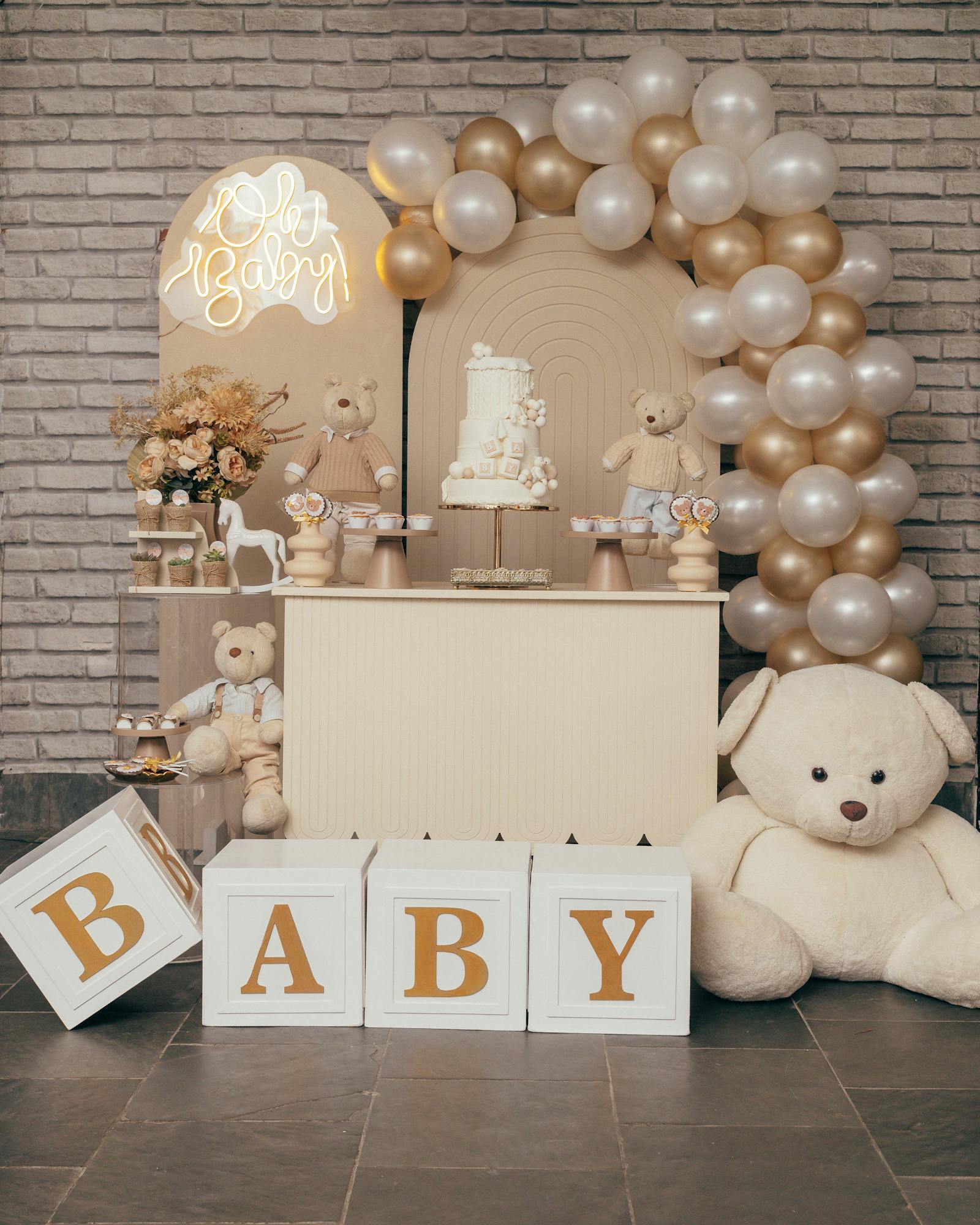 Elegant baby shower setup with Oh Baby balloon arch, cream and gold balloons, and teddy bears