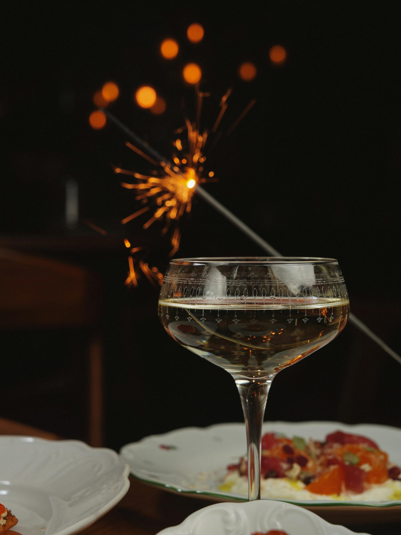 Coupe glass of champagne with lit sparkler over dinner plates